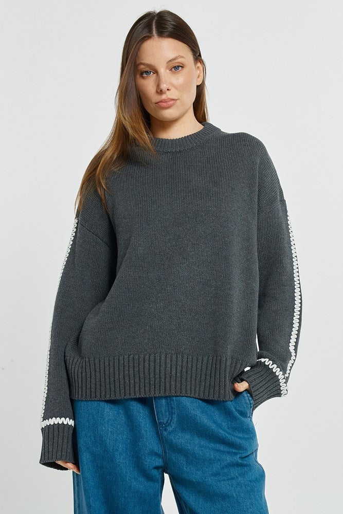 Woman wearing a dark gray sweater with white trim on a light gray background