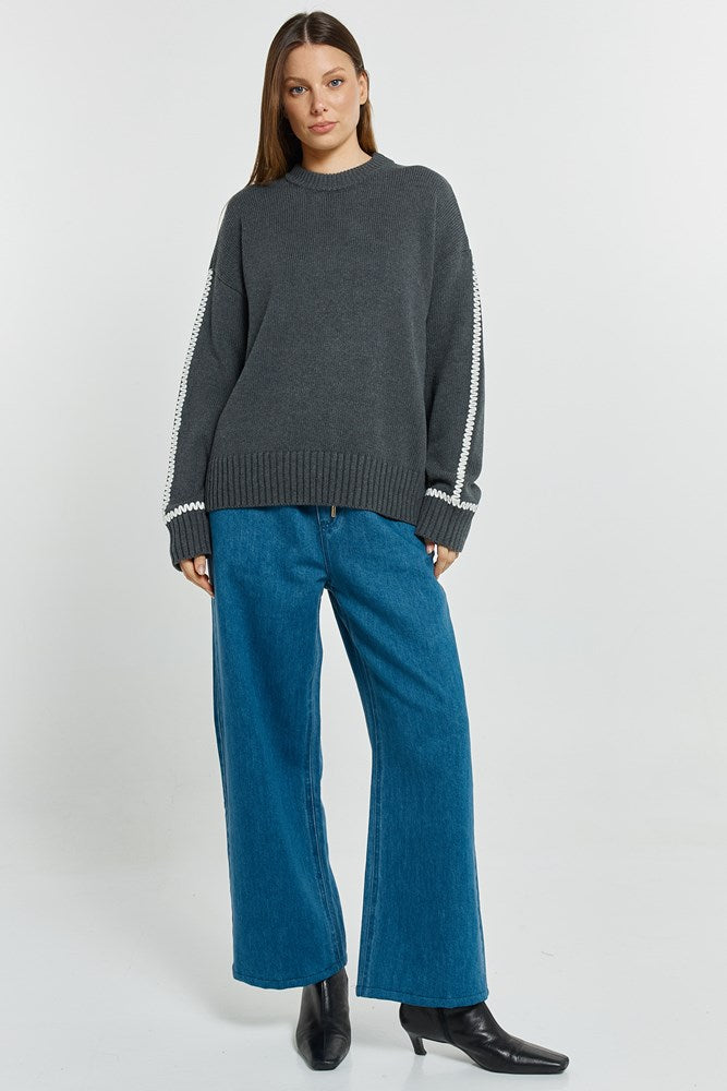 Woman wearing a dark gray sweater with white trim and blue jeans on a white background