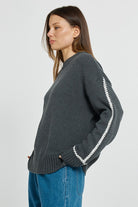 Woman wearing a dark gray sweater with white zipper details on a light gray background