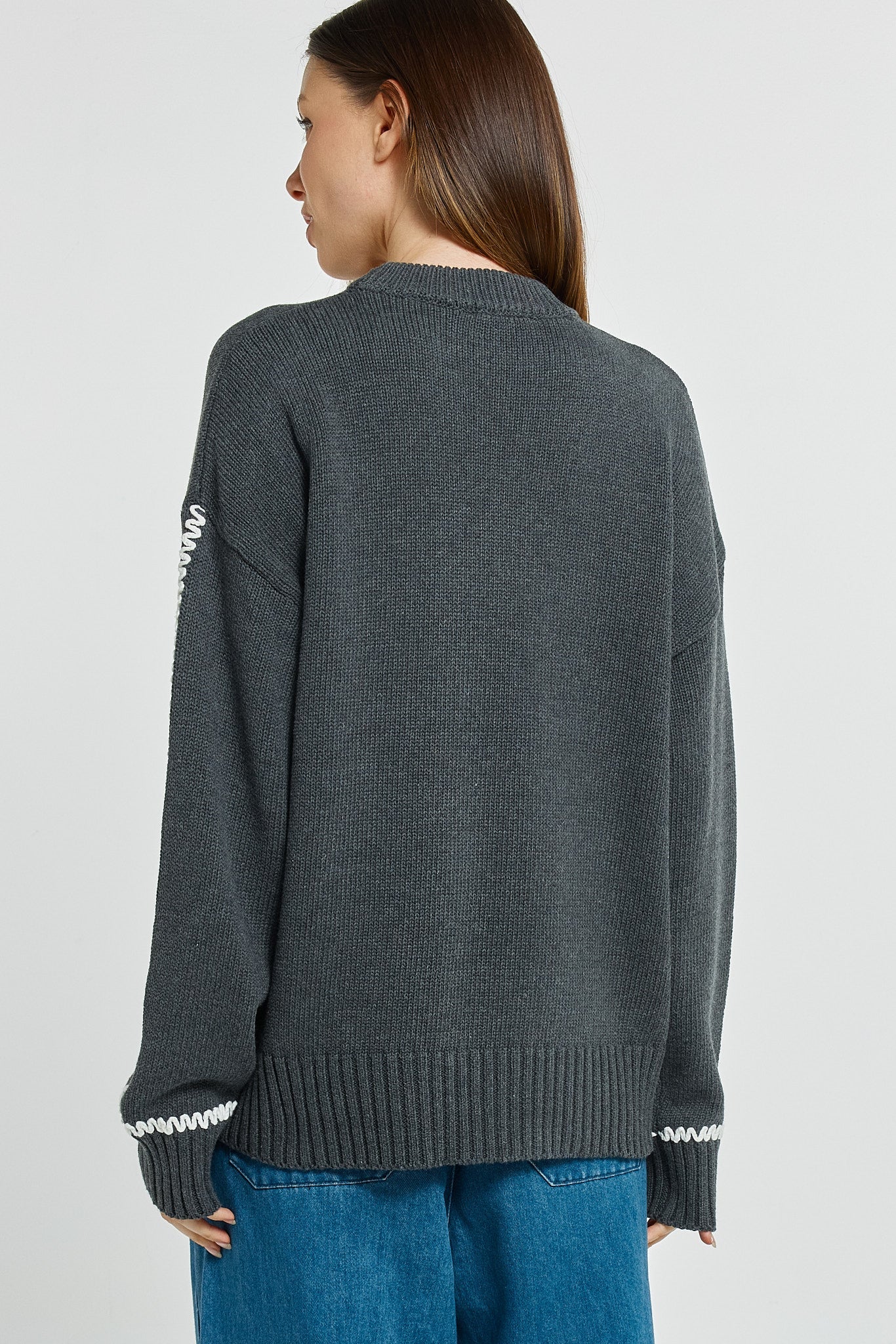 Person wearing a dark gray sweater with white trim on a plain background