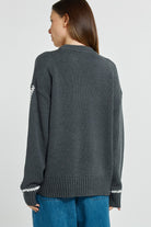 Person wearing a dark gray sweater with white trim on a plain background