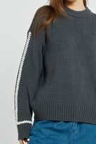Gray sweater with white zipper details worn by a person on a light gray background