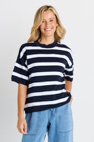 Woman wearing a navy and white striped sweater with blue jeans on a light gray background