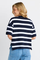 A woman wearing a navy and white horizontally striped knit top, shown from the back against a light gray studio background.