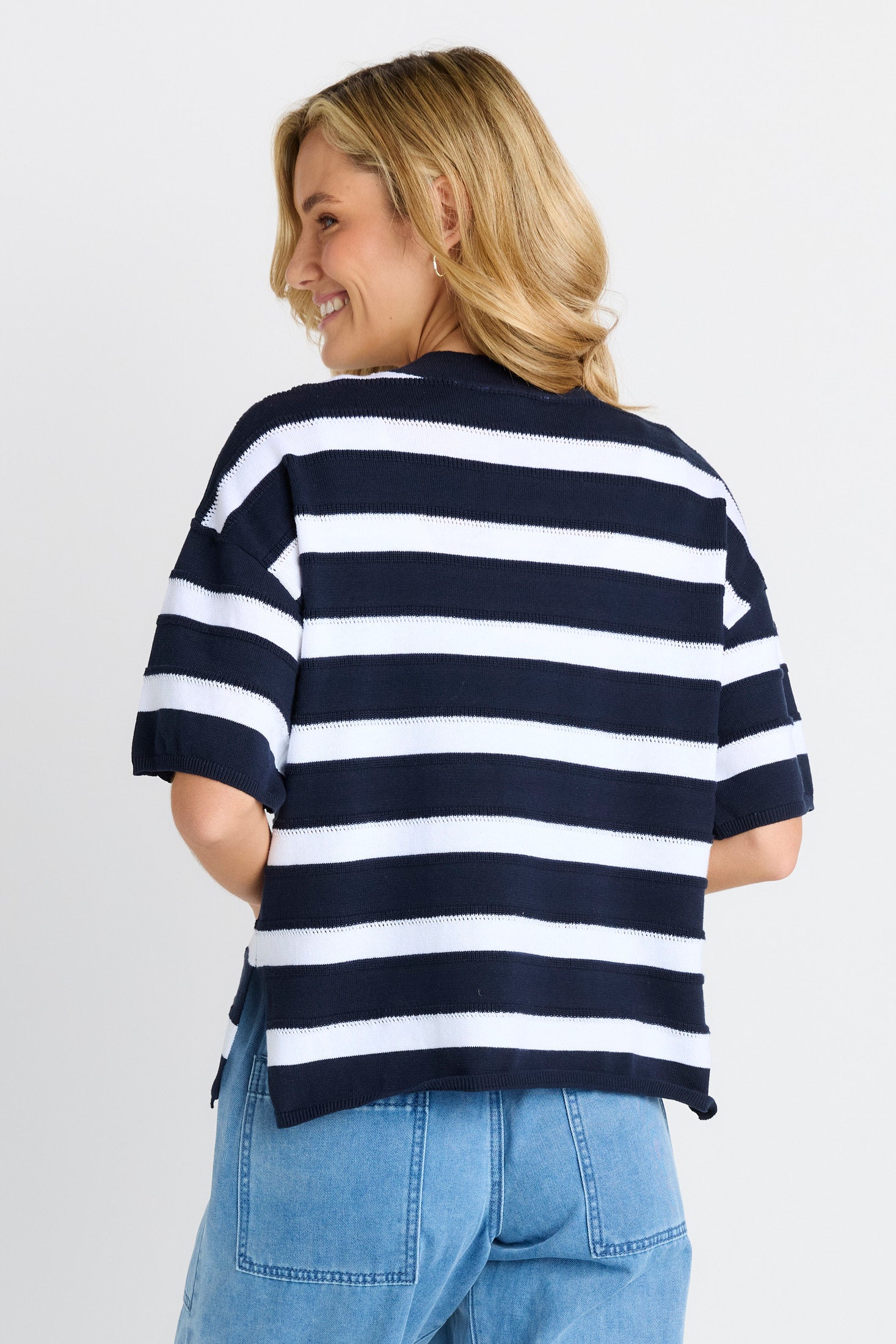 A woman wearing a navy and white horizontally striped knit top, shown from the back against a light gray studio background.