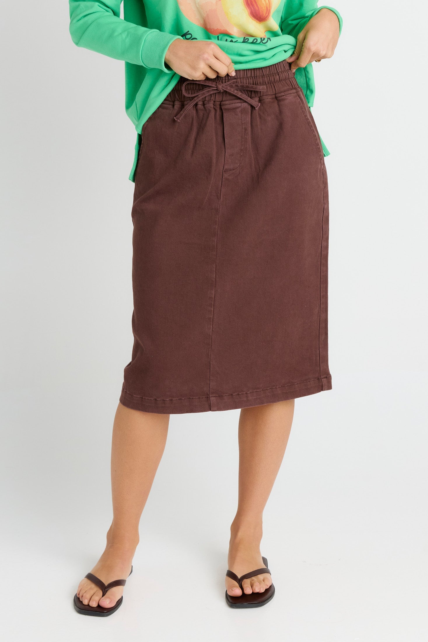 Person wearing a brown skirt and green top on a white background