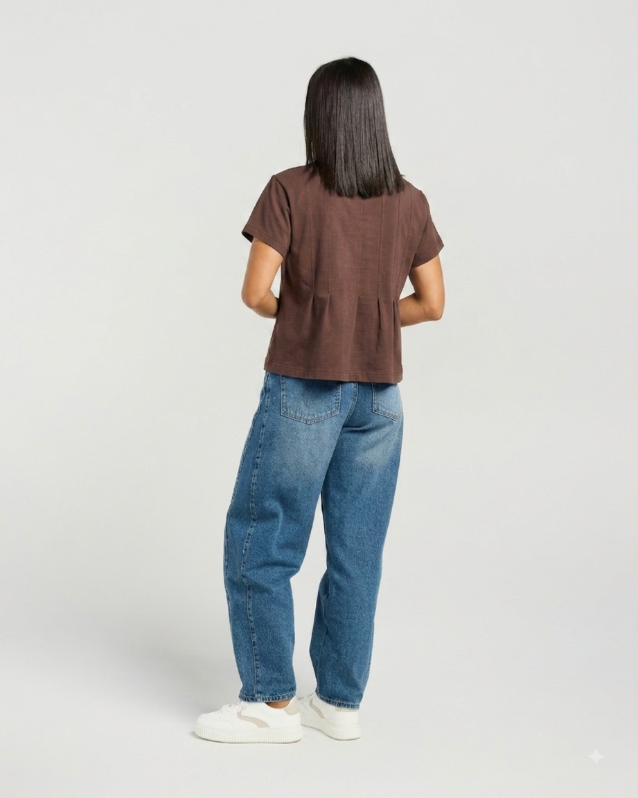 A woman shown from the back wearing a brown short-sleeve cropped top, blue jeans, and white sneakers against a light gray studio background.