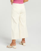 A person shown from the waist down wearing off-white cropped wide-leg pants, a pink ribbed top, and cream block-heel slide sandals against a light gray studio background.
