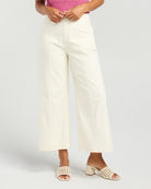 A model wearing off-white wide-leg cropped pants, a pink ribbed top, and cream-colored open-toe heeled sandals with cutout details, set against a plain light gray studio background.
