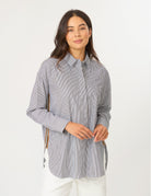 A woman modeling a light gray and white vertically striped button-down shirt with white pants, standing against a plain white studio background.