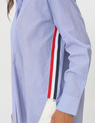 Close-up of a light blue long-sleeve shirt with a vertical red, white, and navy stripe detail on the side, worn by a model.