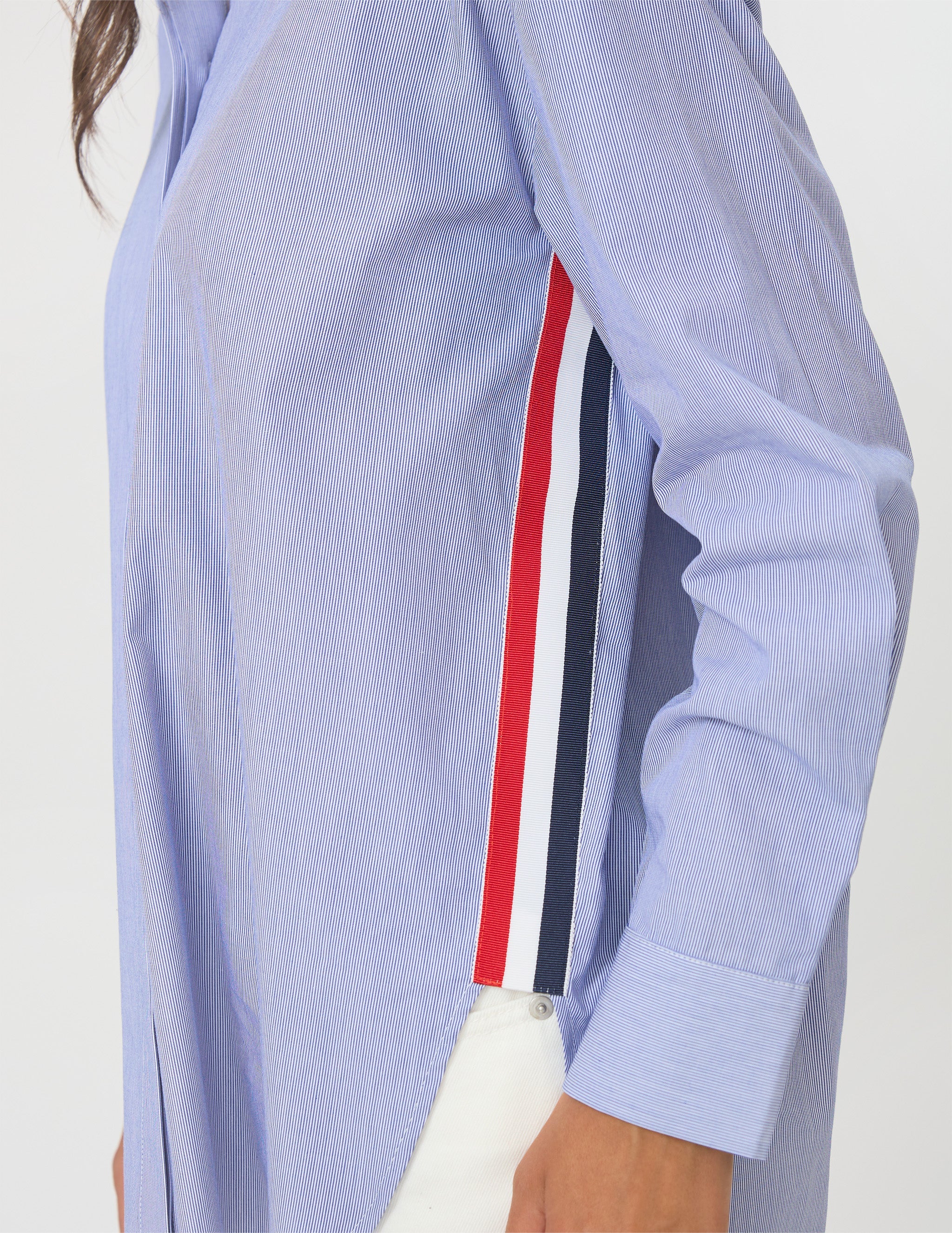 Close-up of a light blue long-sleeve shirt with a vertical red, white, and navy stripe detail on the side, worn by a model.