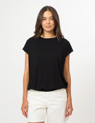 A woman modeling a black short-sleeve crewneck t-shirt paired with white shorts, standing against a plain white studio background.