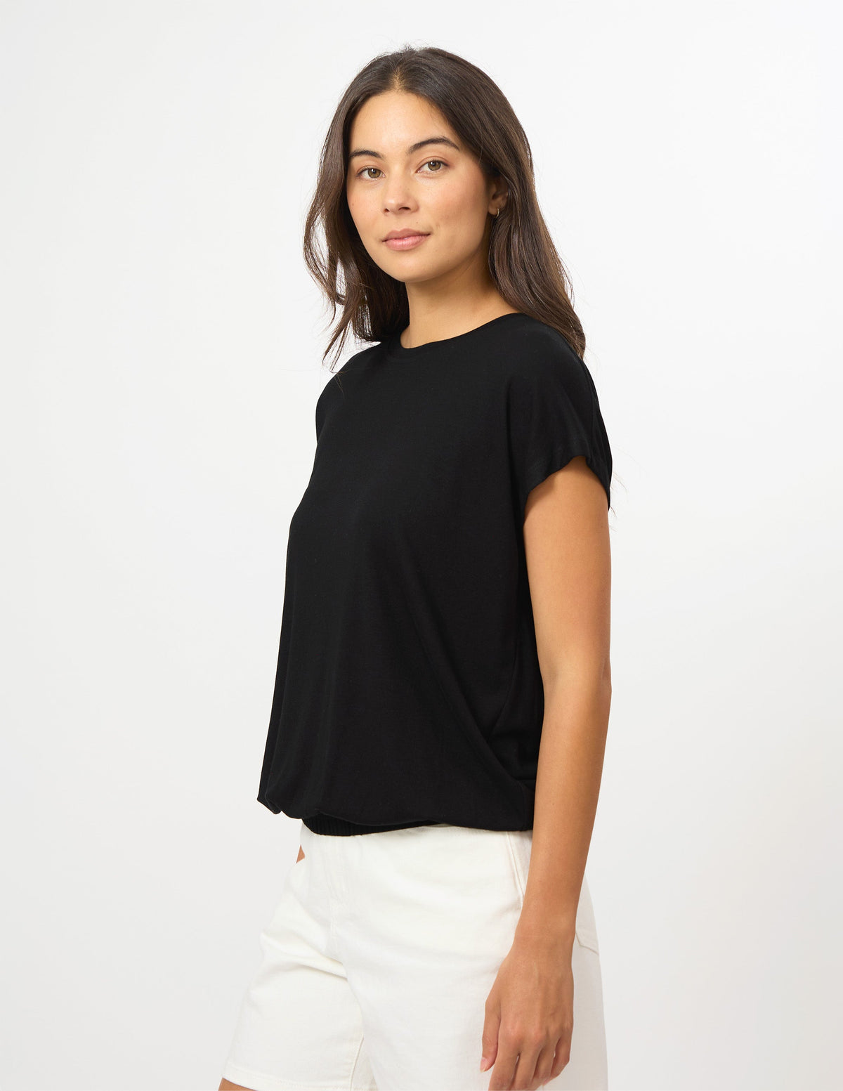 A woman modeling a black short-sleeve crewneck top paired with white shorts, photographed against a clean white studio background.