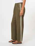 A person wearing olive green wide-leg pants with two vertical white stripes down the side, paired with black flip-flops against a plain white studio background.