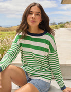 A woman wearing a green and white striped long-sleeve sweater with a navy blue crew neck, sitting outdoors on stone steps.