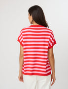 A woman viewed from the back wearing a red and white horizontally striped short-sleeve top and white pants, against a plain light gray studio background.