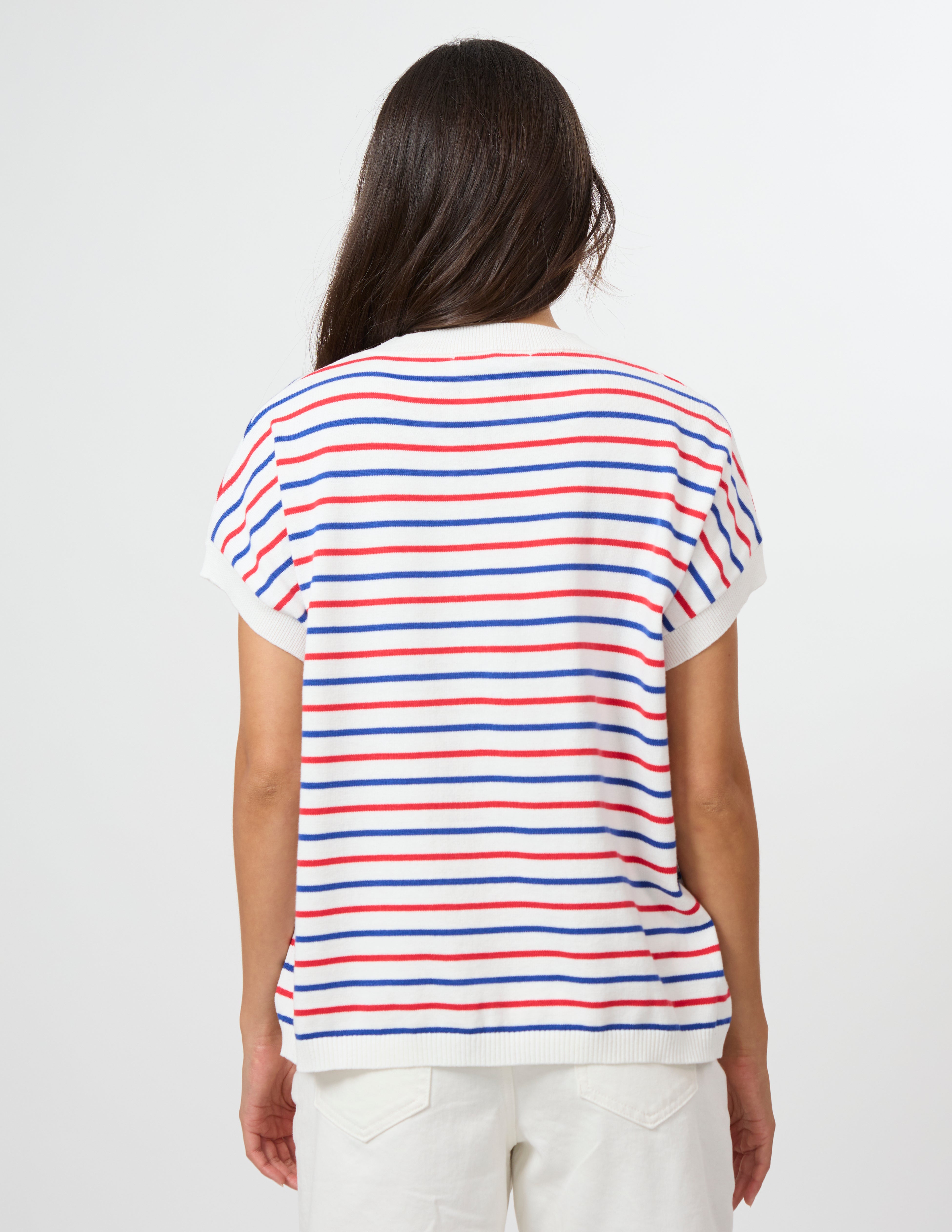 A woman viewed from the back wearing a white short-sleeve T-shirt with thin horizontal red and blue stripes, paired with white pants, against a plain light gray studio background.