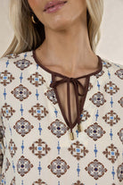 Close-up of a patterned blouse with a tie detail on a neutral background