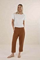 Woman wearing a white top and brown pants on a beige background