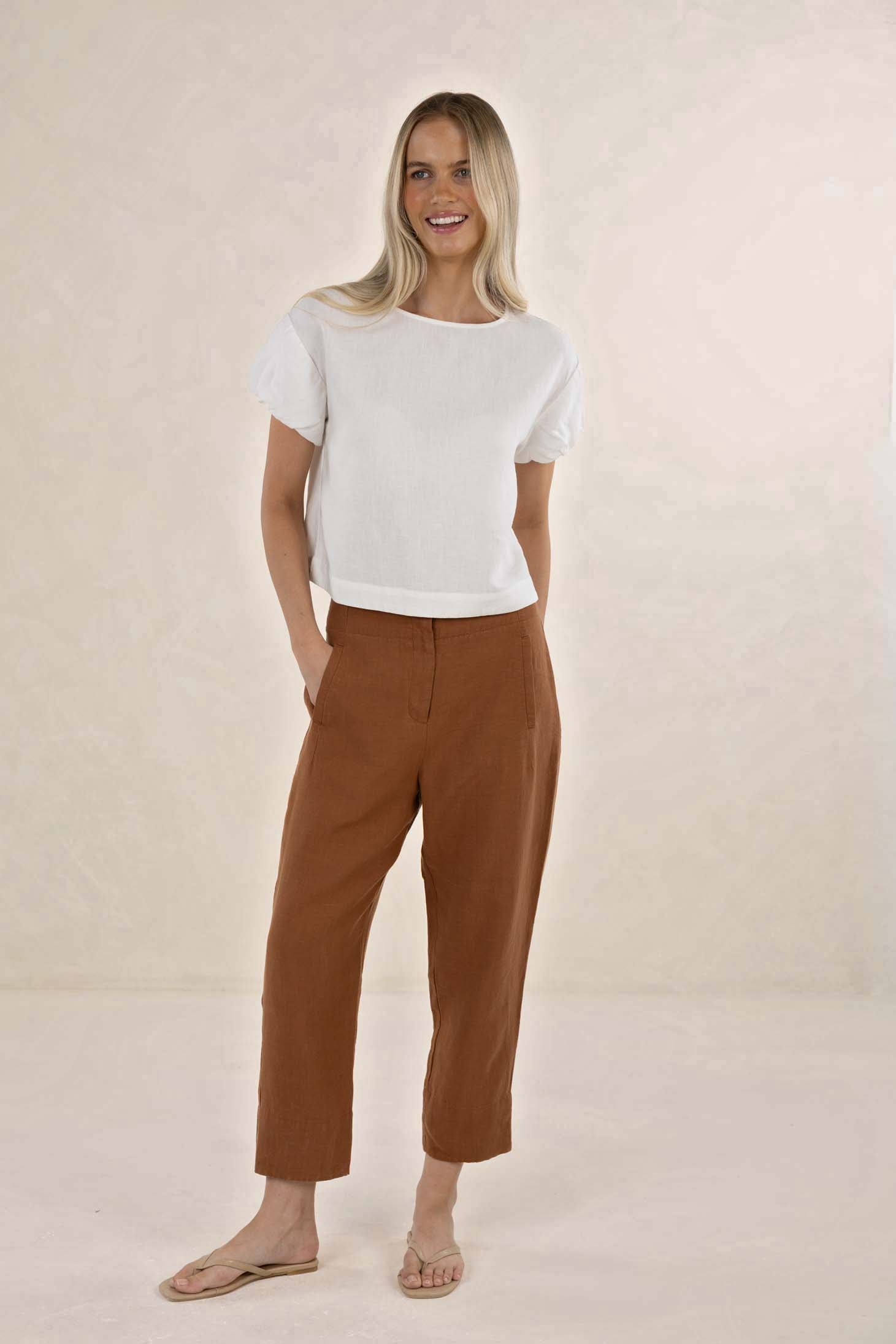 Woman wearing a white top and brown pants on a beige background