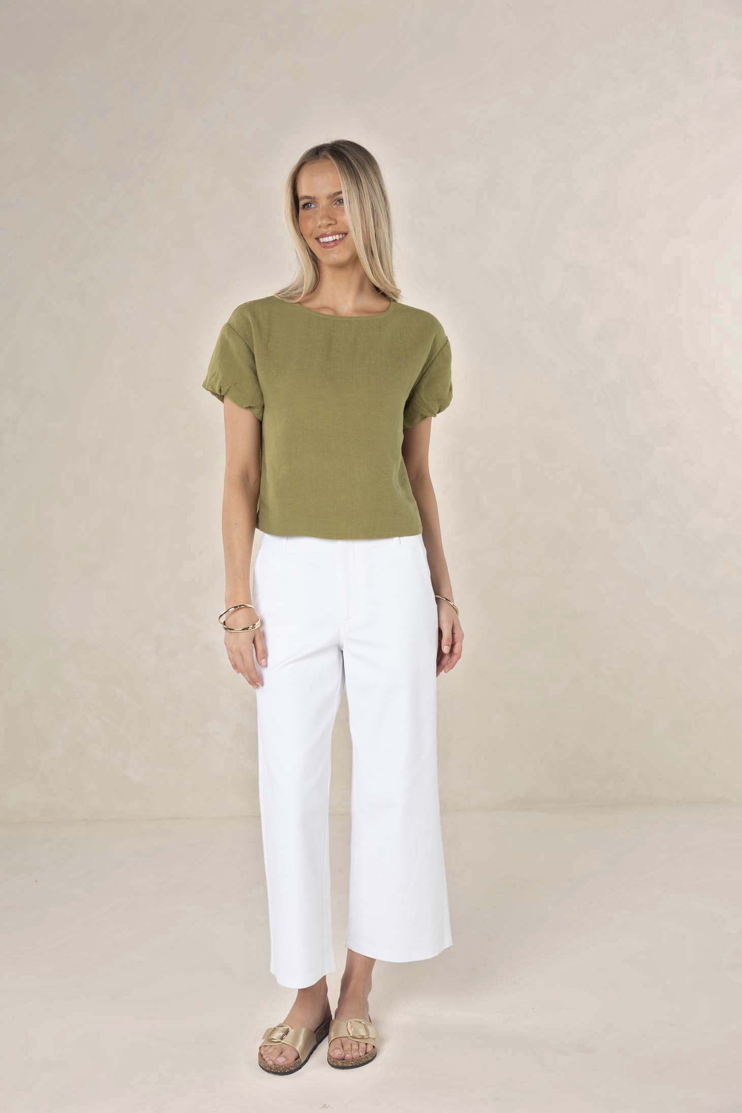 Woman wearing a green top and white pants against a beige background