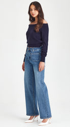 Woman wearing a navy off-shoulder top and blue jeans on a white background