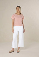 Woman wearing a pink top and white pants on a beige background