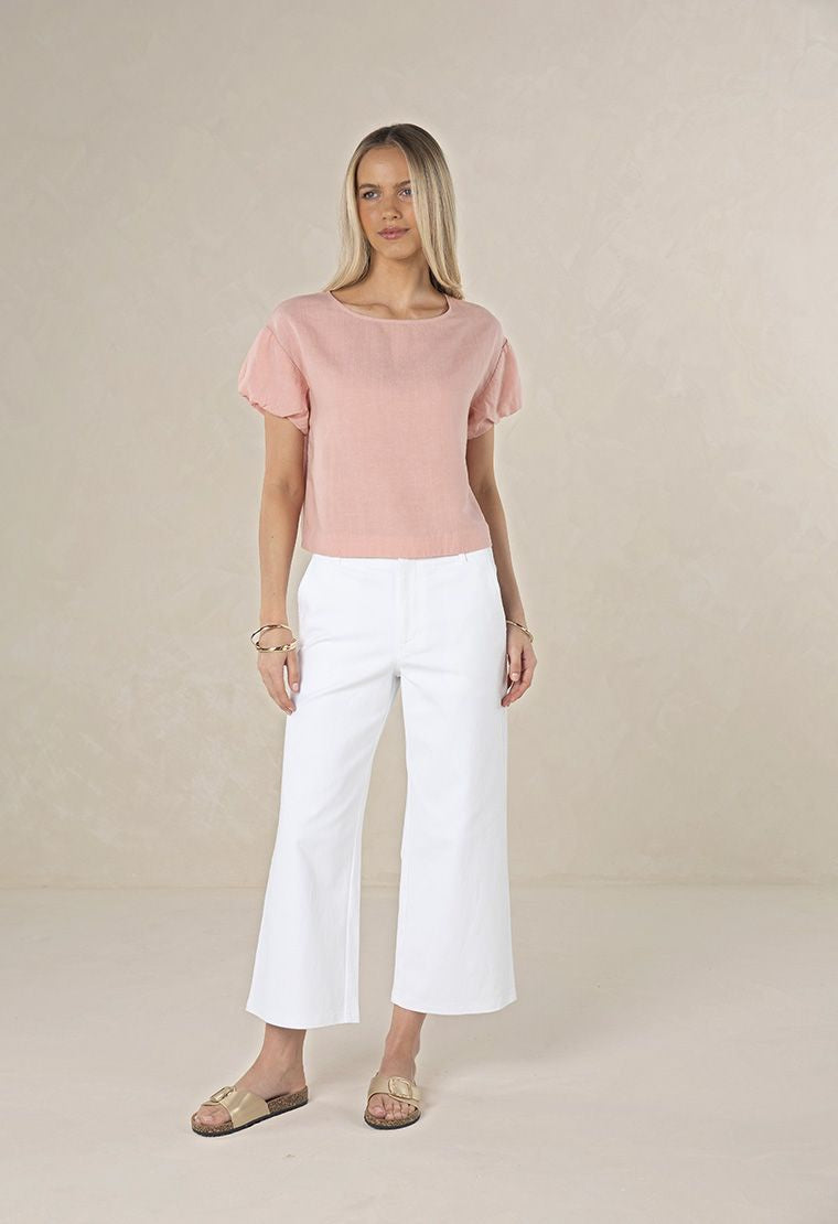Woman wearing a pink top and white pants on a beige background
