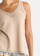 A close-up of a model wearing a light beige knit tank top with a V-neck and ribbed trim, paired with a patterned skirt.