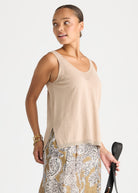 A woman modeling a light beige knit sleeveless top with a V-neck and side slits, paired with a patterned skirt, against a plain light gray studio background.