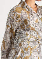 A close-up of a long-sleeve collared shirt dress with a brown and white paisley pattern, shown on a model against a light gray background.