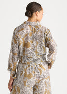 A woman shown from the back wearing a long-sleeve belted jumpsuit with a brown, beige, and white paisley pattern, set against a plain light gray background.