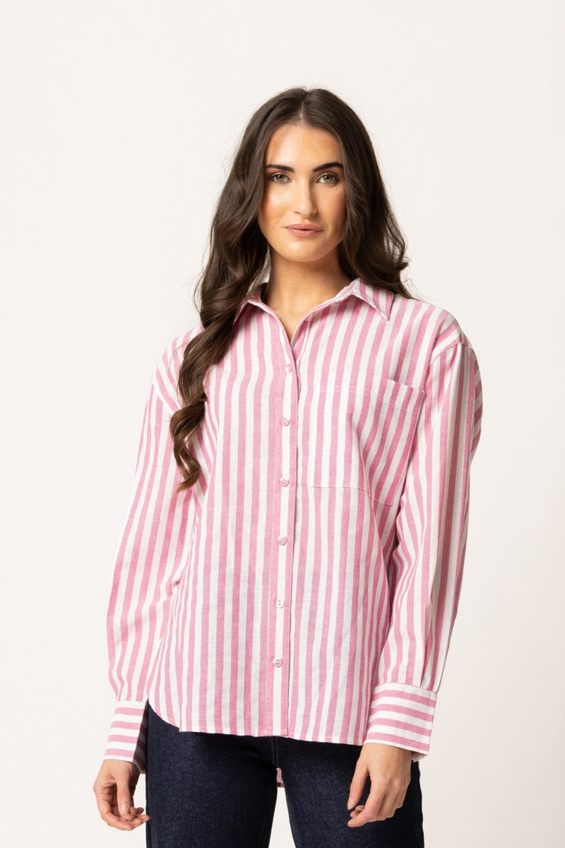 A woman modeling a pink and white vertically striped button-down shirt with dark blue jeans, photographed against a plain off-white studio background.