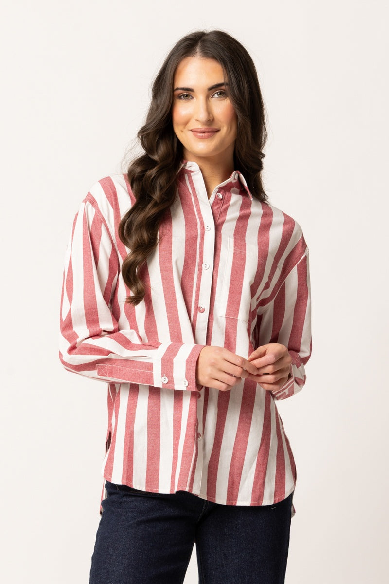 A woman modeling a long-sleeve button-up shirt with vertical red and white stripes, paired with dark blue jeans, against a plain light background.