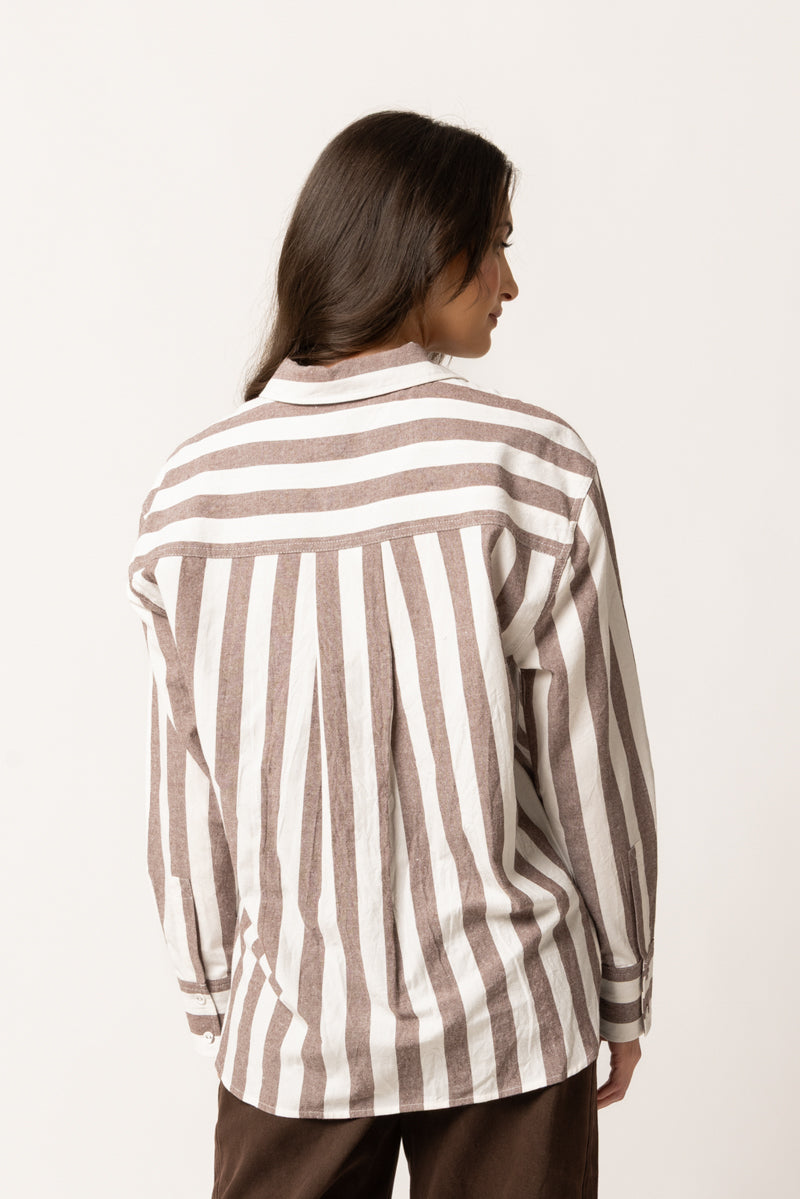 A model shown from the back wearing a long-sleeve button-up shirt with vertical brown and off-white stripes, paired with dark brown pants, against a plain off-white background.
