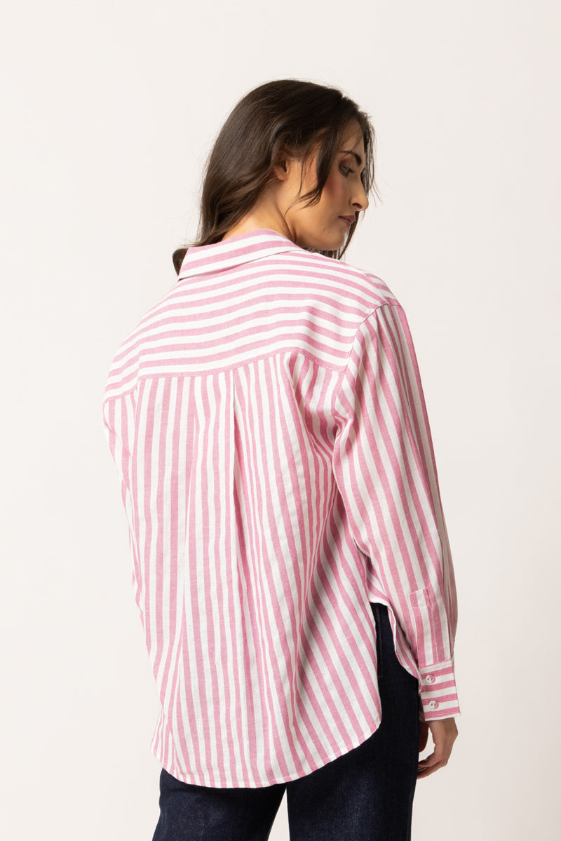 A woman shown from the back wearing a pink and white vertically striped button-up shirt and dark jeans, photographed against a plain light background.
