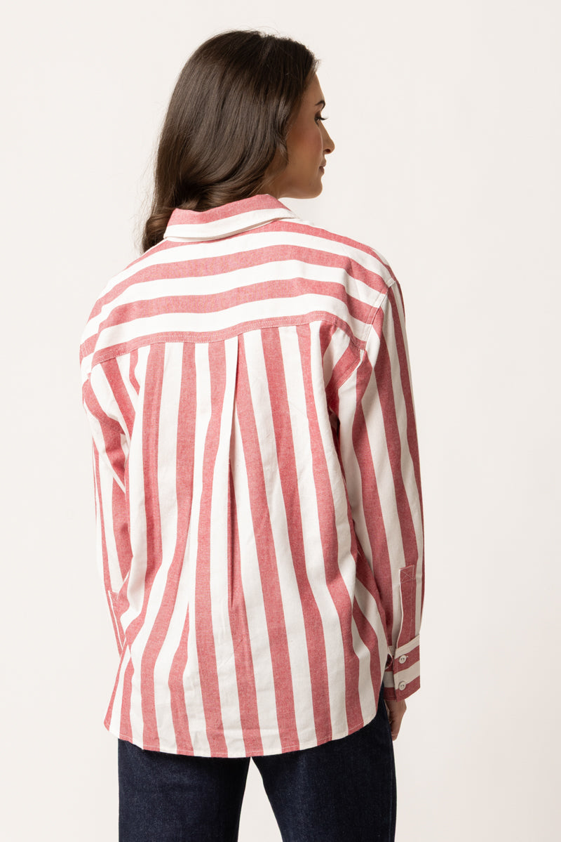 A woman shown from the back wearing a pink and white vertically striped button-up shirt and dark blue jeans, photographed against a plain off-white studio background.