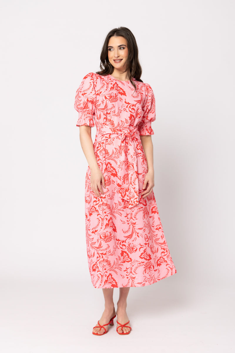 women wearing a pink floral dress in front of a neutral background.
