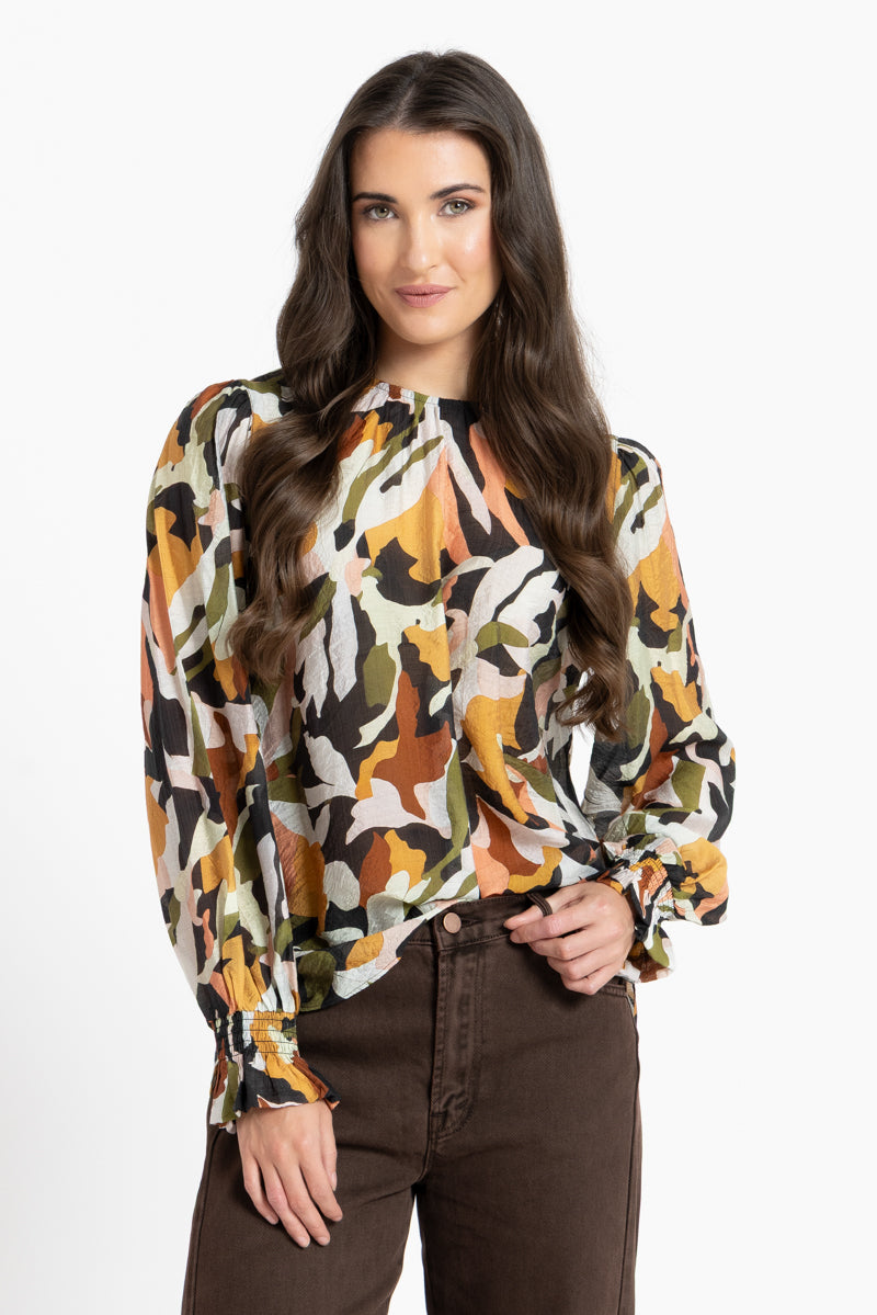 Woman wearing a long-sleeve, patterned blouse with autumn colors on a white background