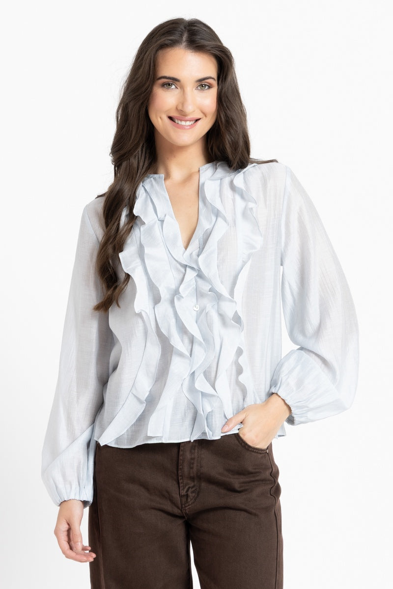 Woman wearing a light blue blouse with ruffled details on a white background