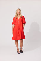 A woman modeling a bright red short-sleeve button-front dress with puff sleeves, paired with black strappy heels, against a light gray studio background.