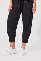 A person wearing loose black cropped pants with elastic cuffs and white platform sneakers, photographed against a clean light gray studio background.