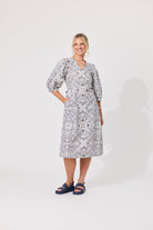 A woman modeling a knee-length dress with a blue and white floral pattern, featuring puff sleeves and a V-neckline, standing against a plain light gray studio background.