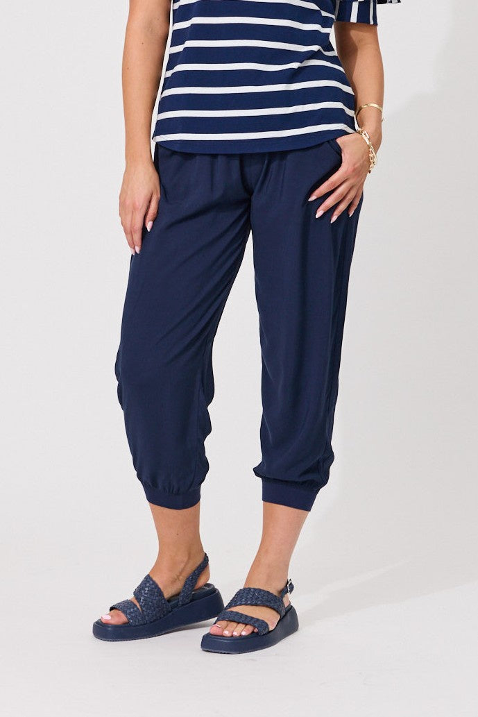 A model wearing navy blue cropped jogger pants, a navy and white striped t-shirt, and matching navy sandals, shown from the waist down against a light gray studio background.