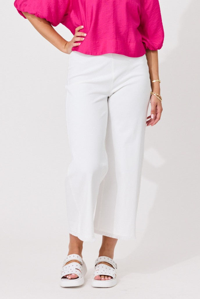 A model wearing white cropped wide-leg pants, a bright pink puff-sleeve top, and white platform sandals, standing against a plain white studio background.