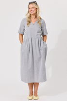A woman modeling a short-sleeve midi dress with a small black and white gingham pattern, standing against a plain white studio background.