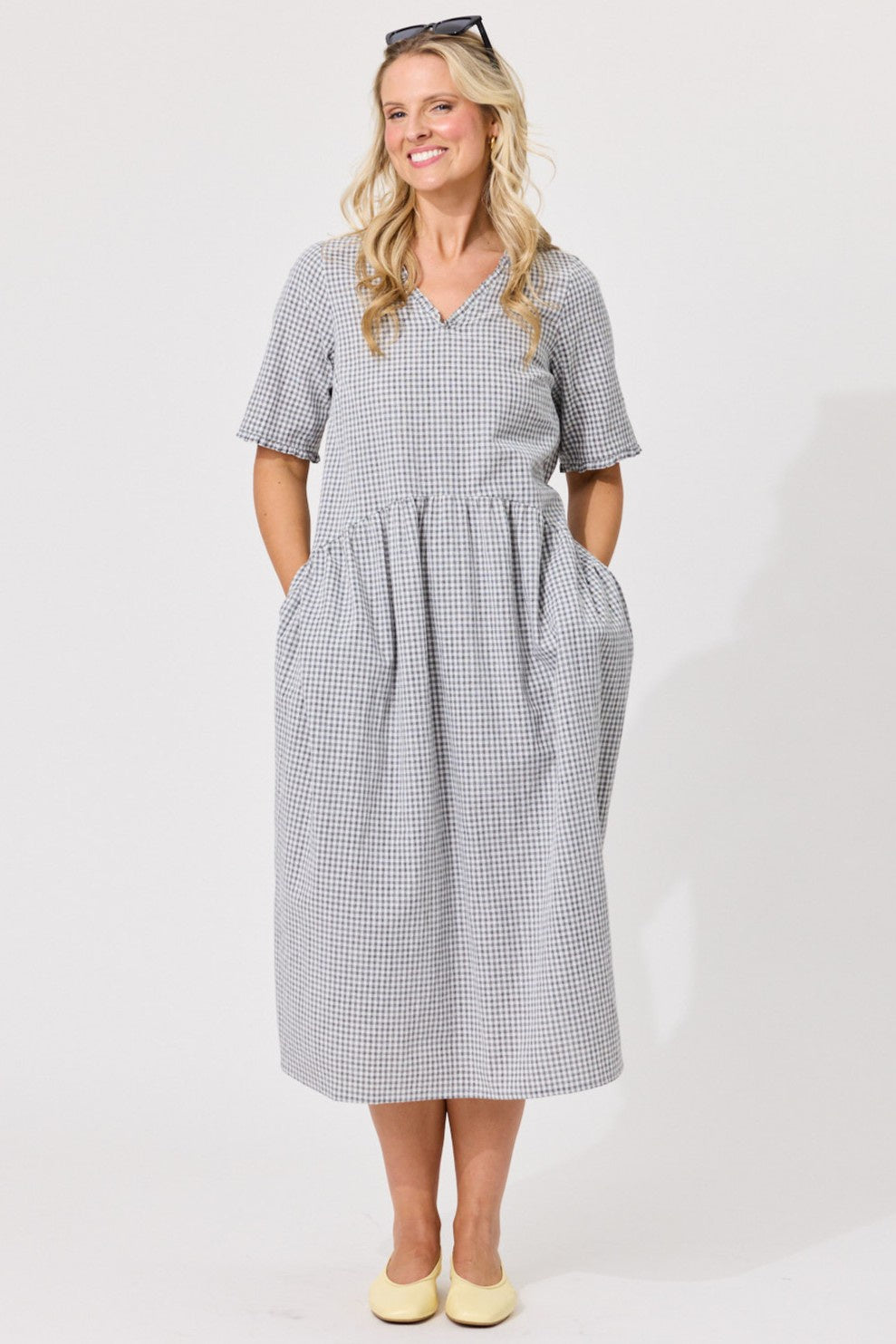 A woman modeling a short-sleeve midi dress with a small black and white gingham pattern, standing against a plain white studio background.