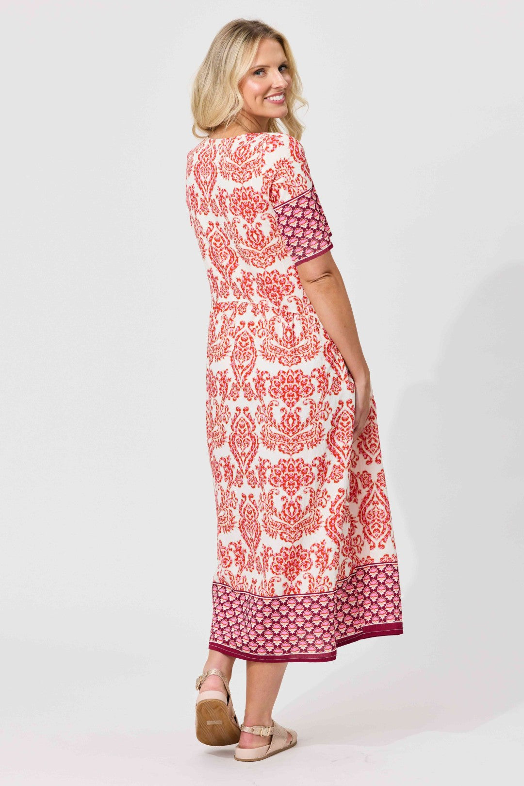 A woman modeling a knee-length dress with a red and white patterned print, shown from a three-quarter back angle against a light gray studio background.