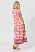 A woman modeling a knee-length dress with a red and white patterned print, shown from a three-quarter back angle against a light gray studio background.
